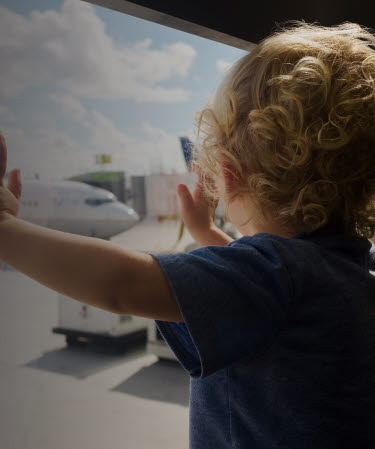 Toddler standing by a window looking at an airplane.
