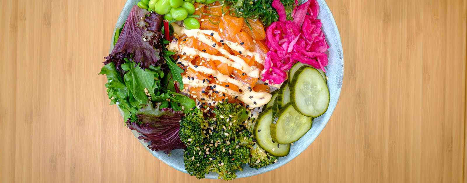 Bowl with broccoli, salad, edamame beans, cucumber, pickled onion, seaweed and salmon.