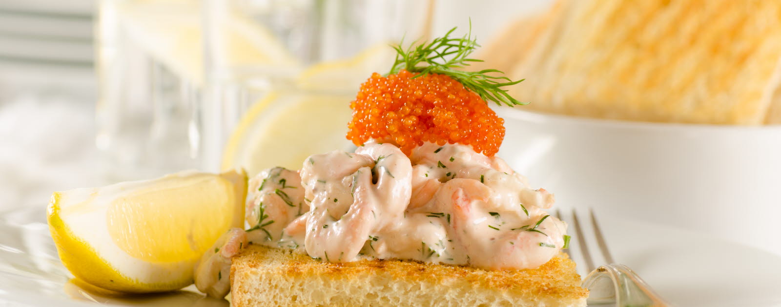 Toast with a creamy shrimp salad and roe with a lemon slice on the side on a plate.
