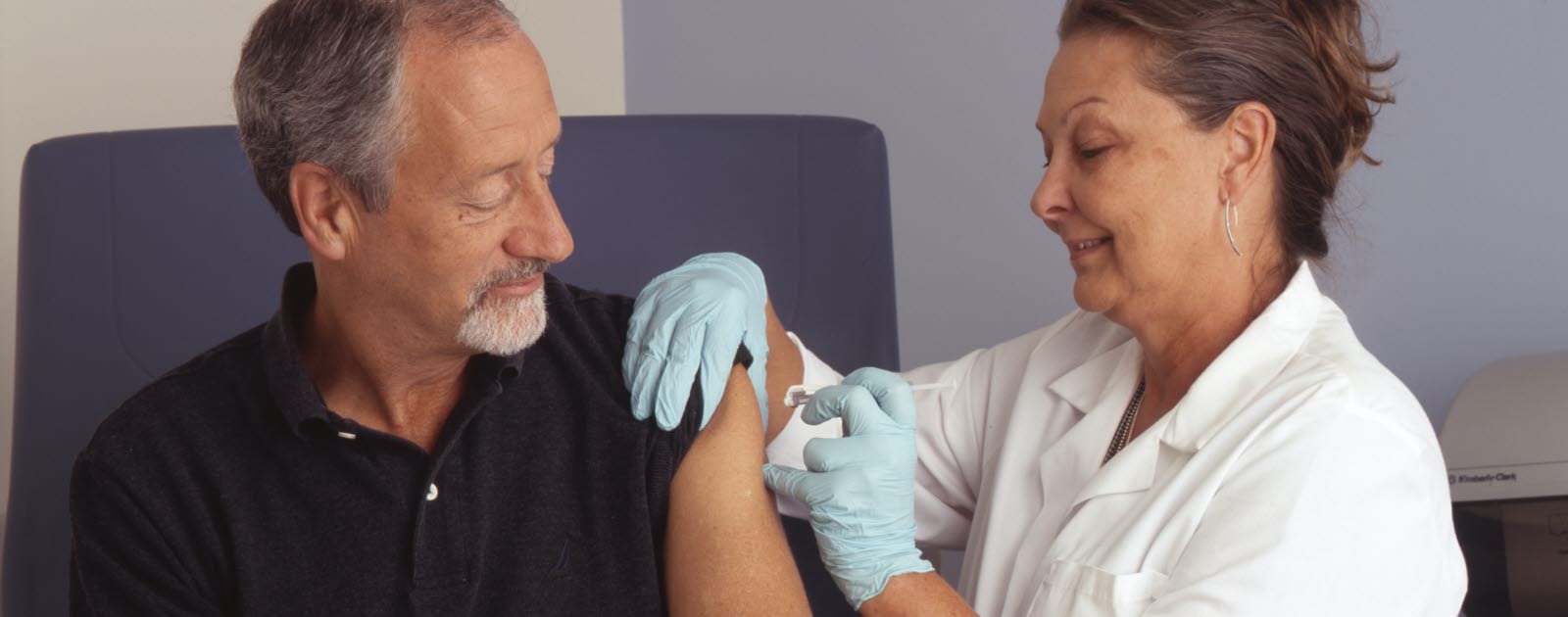 A female nurse administers vaccination into a male patient's arm as he watches.
