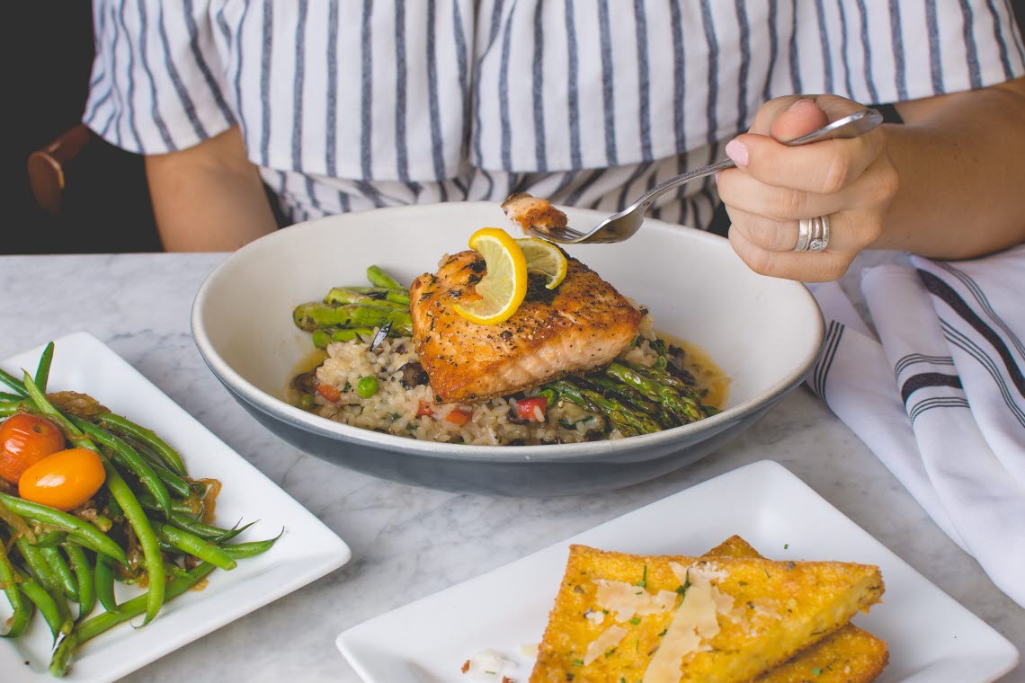 Woman eating a dinner of salmon, asparagus, couscous, garlic bread and greens.