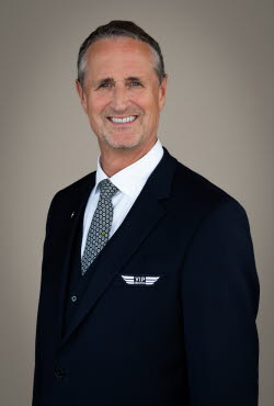 Man with grey hair and stubble dressed in suit and tie smiling at the camera.
