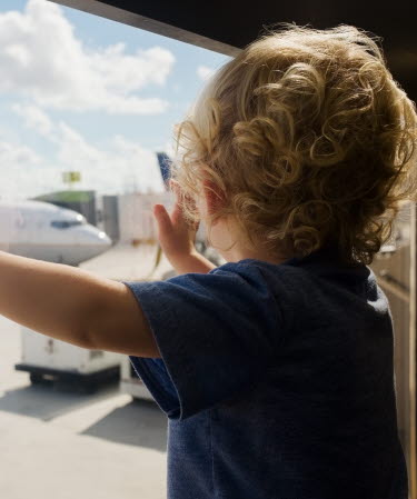 Litet barn står vid ett fönster och tittar på ett flygplan.