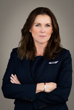 Woman with shoulder length hair dressed in suit jacket is looking at camera while crossing her arms.