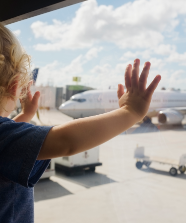 Toddler standing at a window looking at an airplane.
