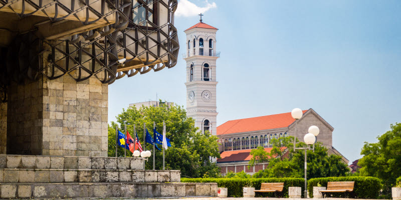 En kyrka och en stenbyggnad bredvid flaggstänger i Pristina