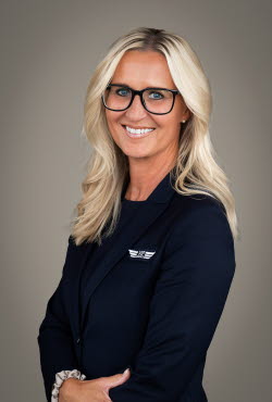 Woman with long hair and glasses dressed in suit jacket smiling at the camera.