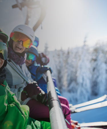 Family wearing ski equipment sitting in chair lift smiling at the camera.