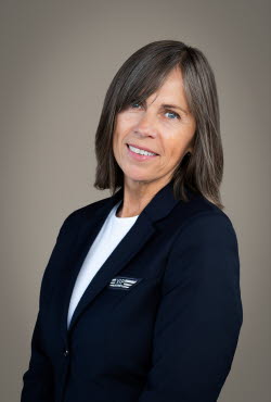Woman with shoulder length hair dressed in suit jacket has her head cocked and smiling at the camera.