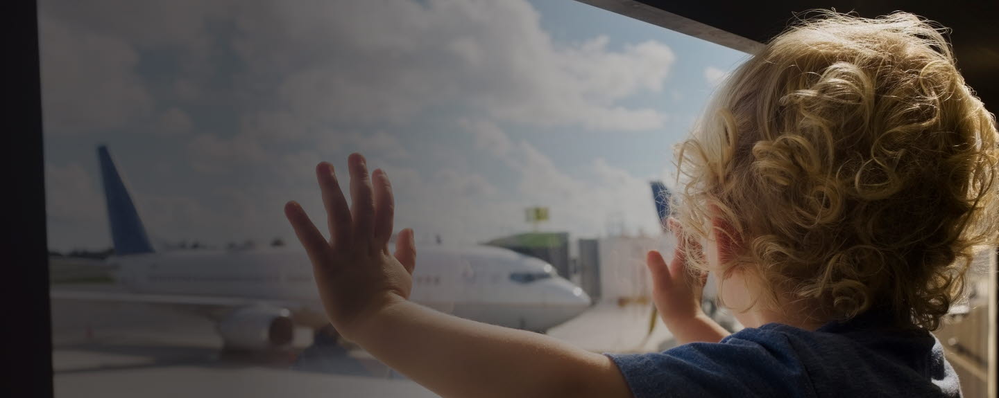 Toddler standing by a window looking at an airplane.