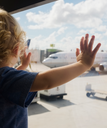 Toddler standing at a window looking at an airplane.