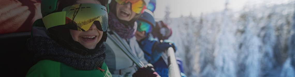 Family wearing ski equipment sitting in chair lift smiling at the camera.