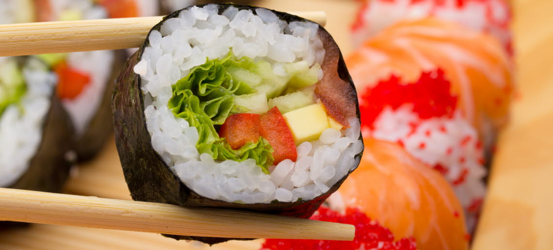 Ätpinnar håller en vegetarisk sushi-rulle över en tallrik med mer sushi.