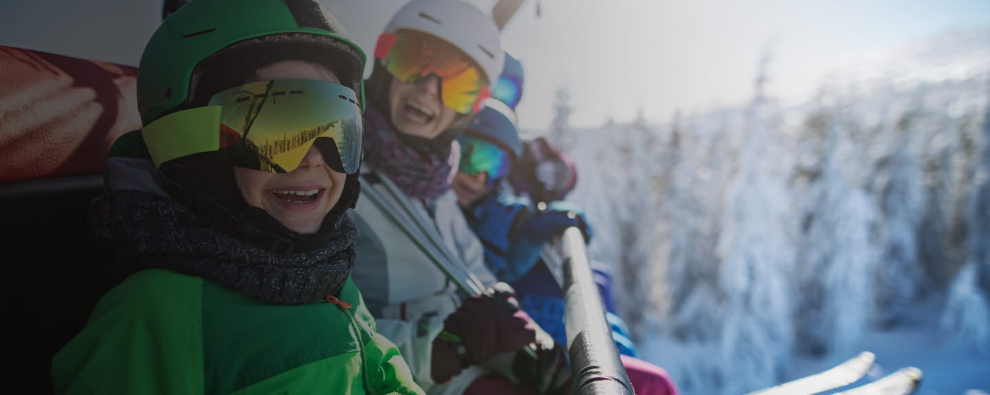 Family wearing ski equipment sitting in chair lift smiling at the camera.
