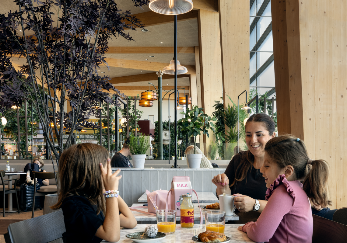 Kvinna och två barn äter mat på en restaurang på flygplatsen 