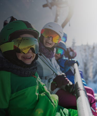 Family wearing ski equipment sitting in chair lift smiling at the camera.