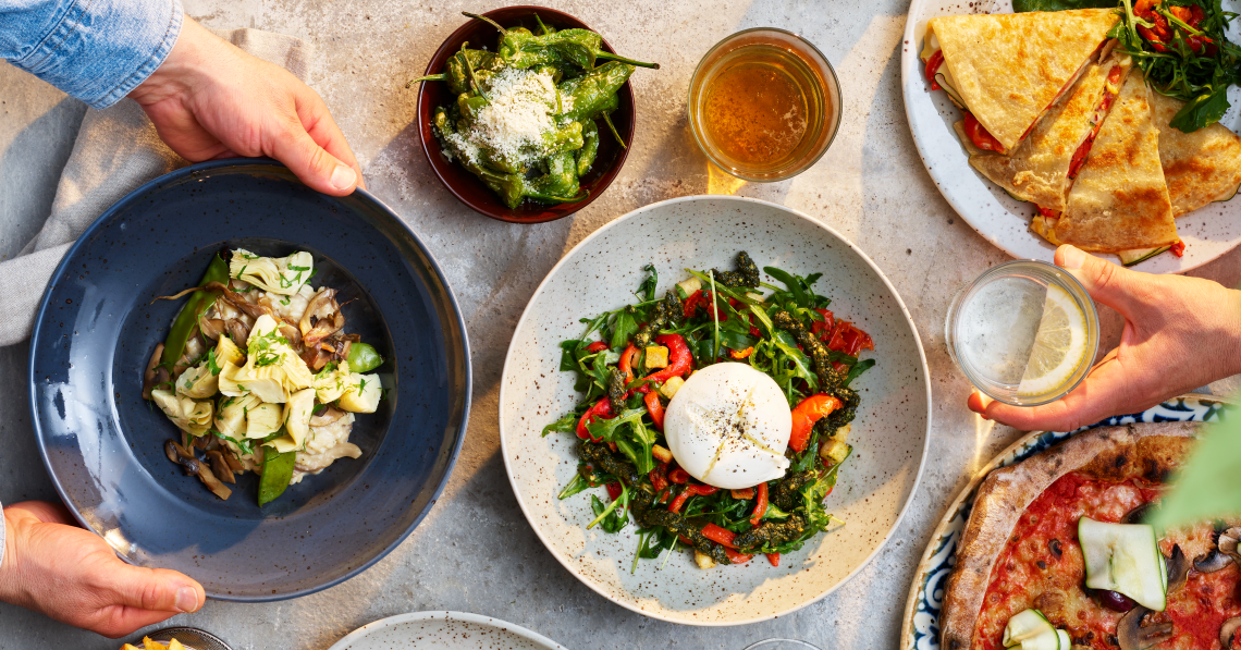 Plates and bowls with colourful meals against a concrete background.