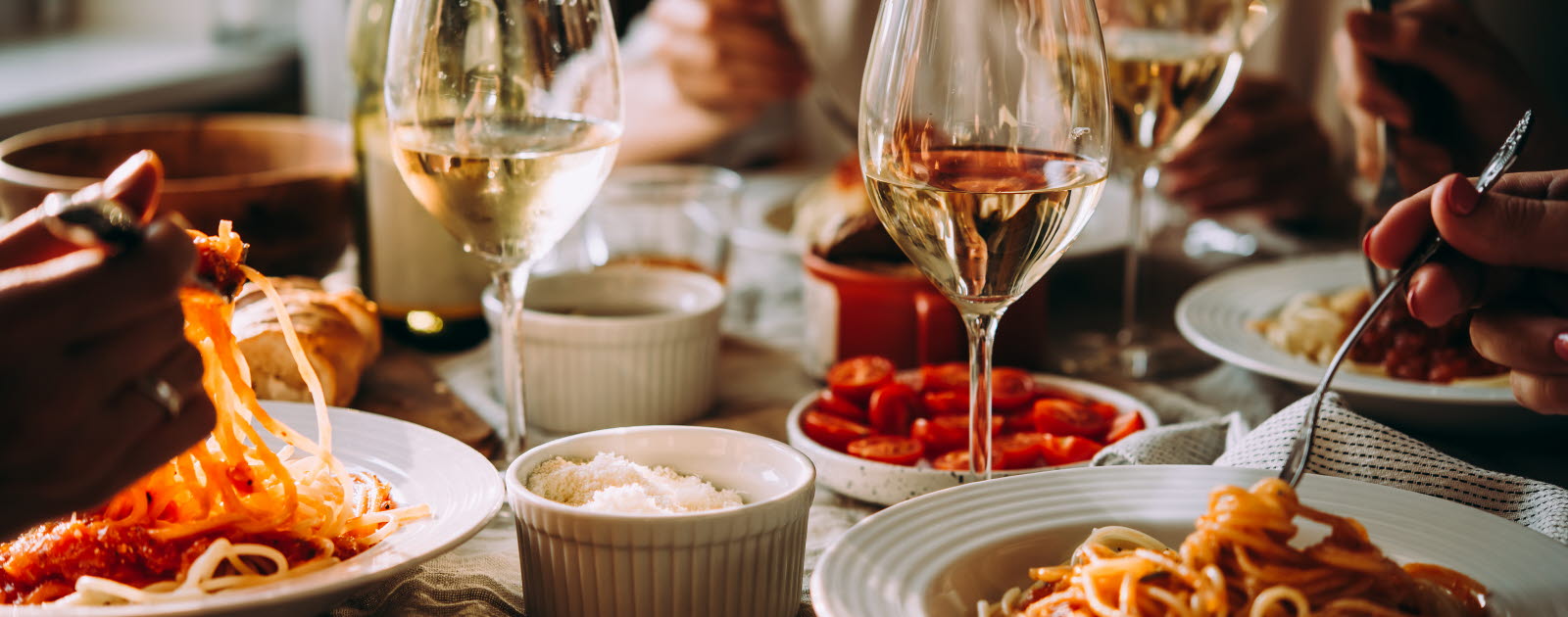 Tallrikar med pastarätter och glas med vitt vin på ett bord.