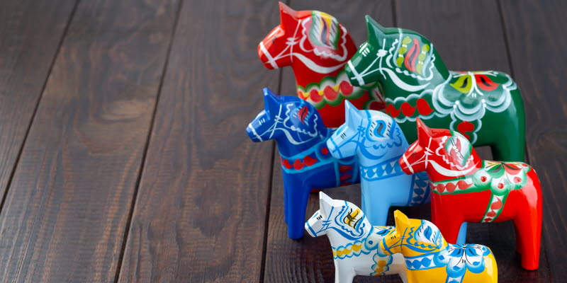 7 dalahästar i olika storlekar och färger på ett trägolv.