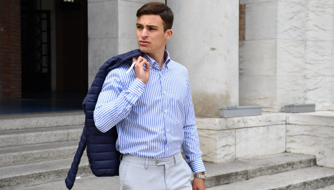 Young man in striped blue/white dress shirt holding jacket over one shoulder.
