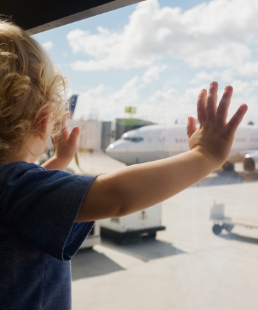 Toddler standing at a window looking at an airplane.