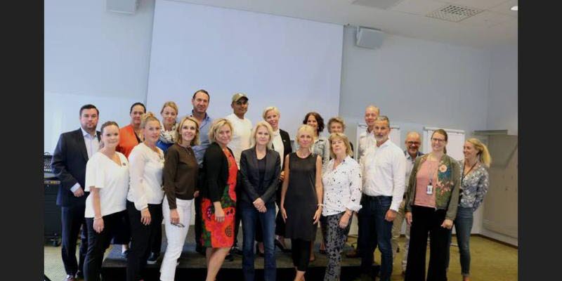 Twenty people  standing in front of a white wall