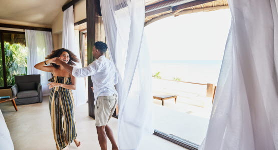Man and woman dancing in front of open balcony doors leading out to the beach.