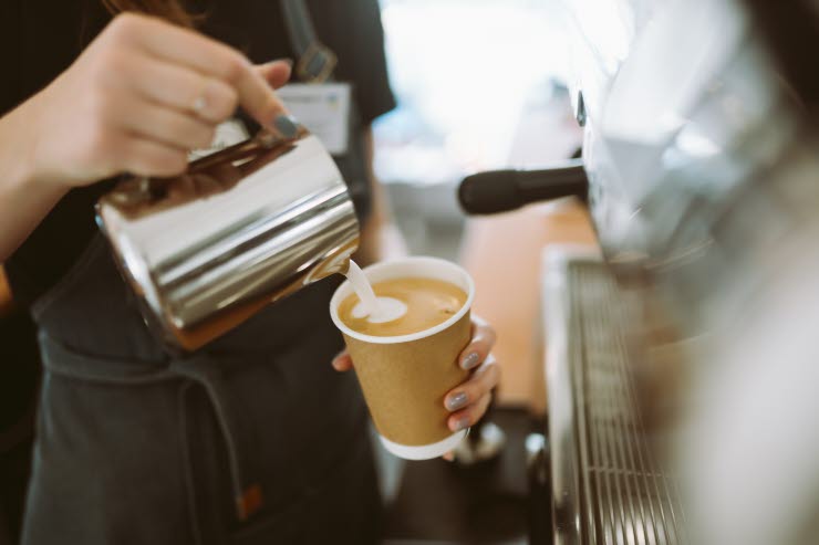 Barista häller skummad mjölk i en take-away-kopp.