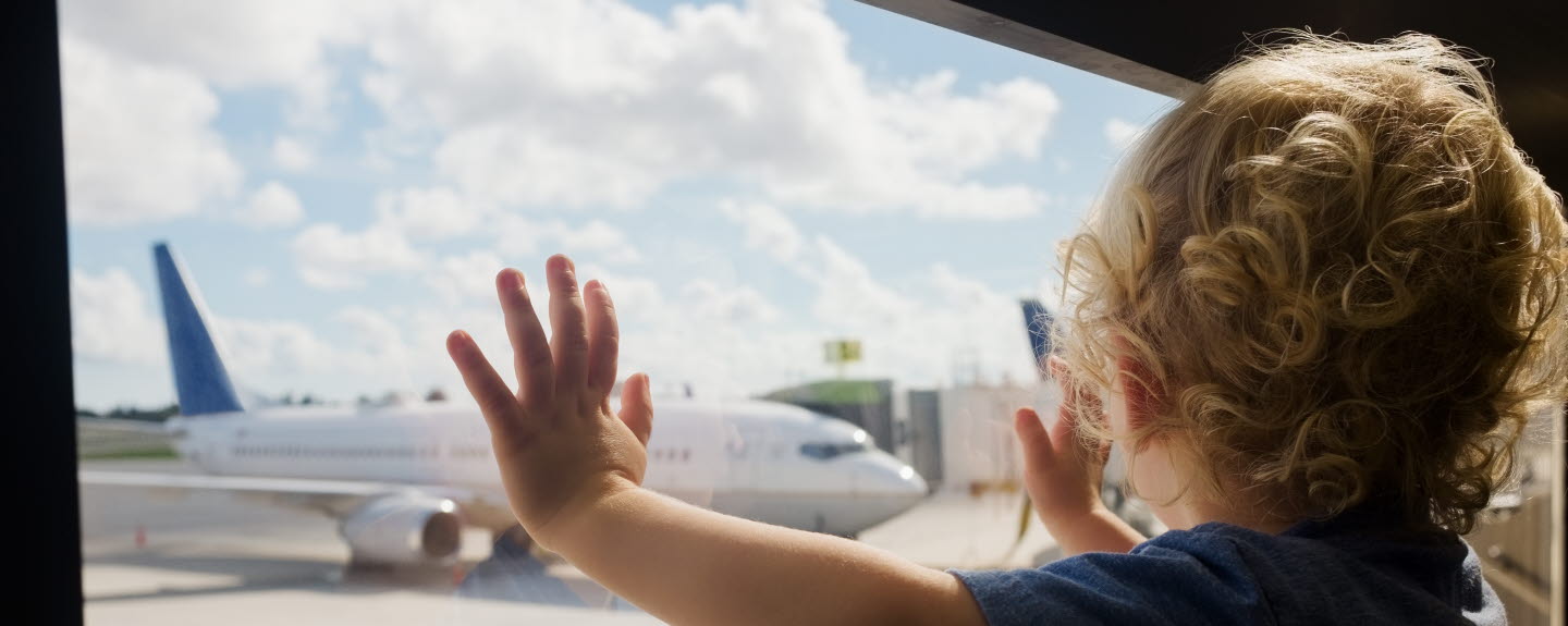 Toddler standing at a window looking at an airplane.