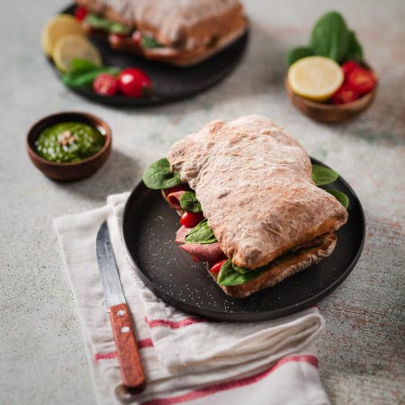 Två ciabattas med kött och grönt, med en grön sås vid sidan.