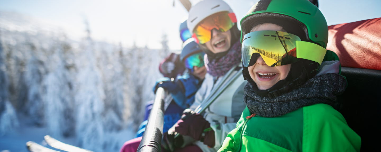 Family in ski equipment sitting in chair lift smiling at the camera.