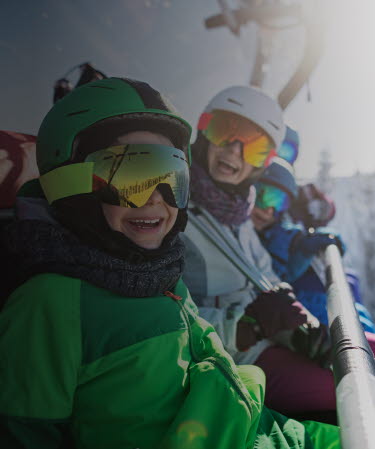 Family wearing ski equipment sitting in chair lift smiling at the camera.