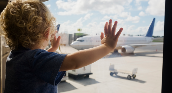 Litet barn står vid ett fönster och tittar på ett flygplan.