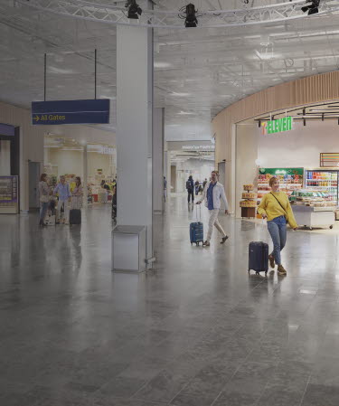 People with suitcases walking and standing in open area between stores.