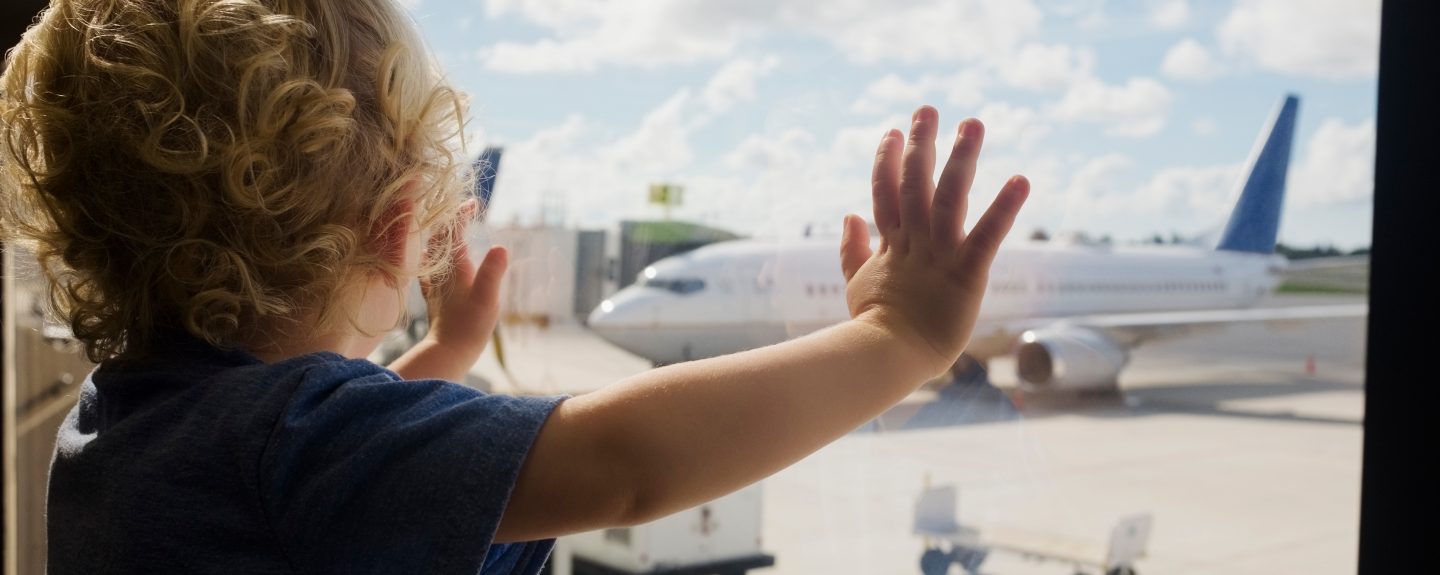 Toddler standing at a window looking at an airplane.