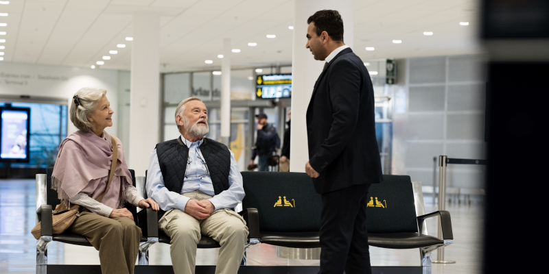 An elderly couple sitting and a man standing