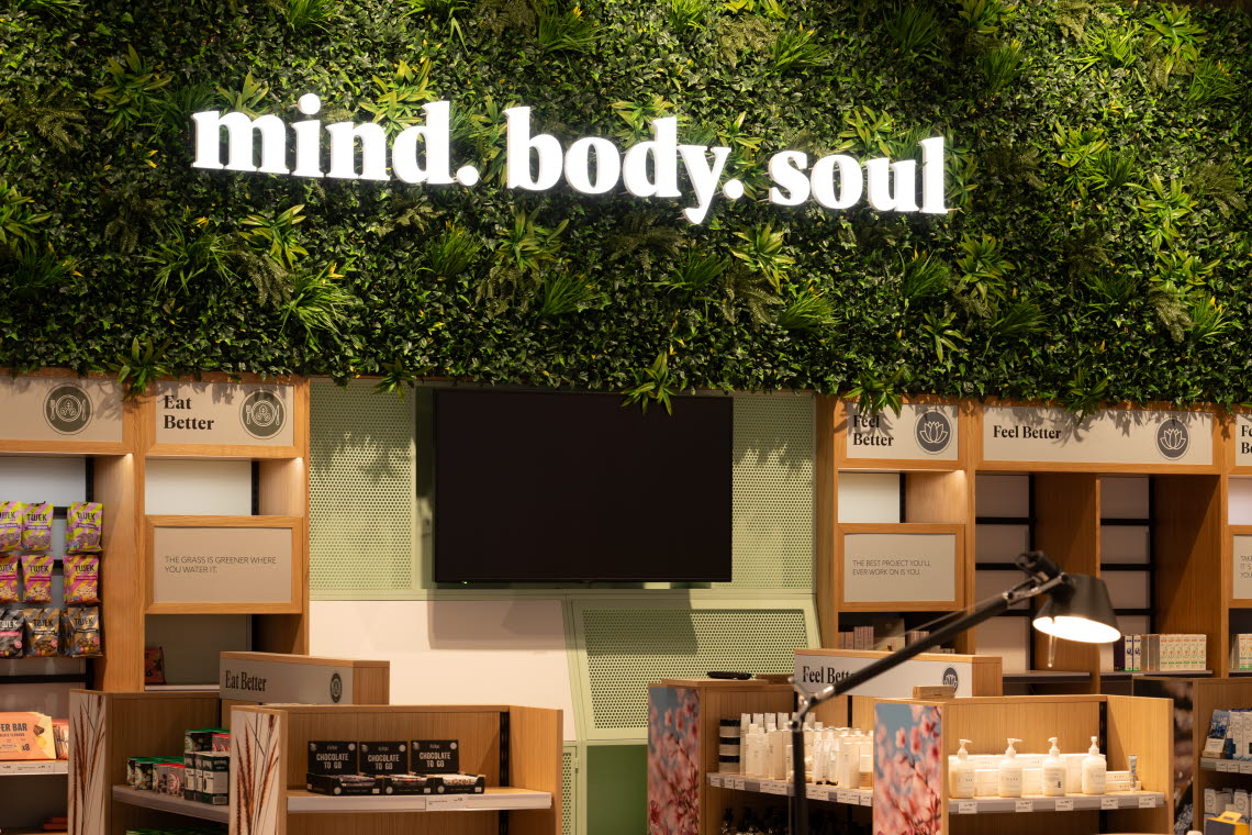 Hyllor i ljust trä fulla med produkter, under växtlighet med en skylt som säger "mind. body. soul.".
