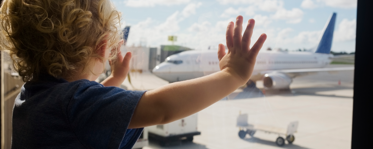 Toddler standing at a window looking at an airplane.