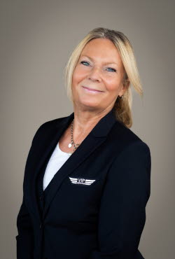 Woman with tied back hair dressed in a suit jacket smiling at the camera.