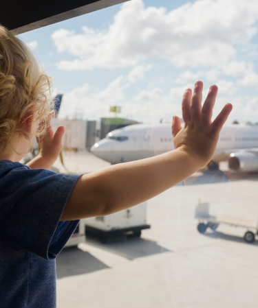 Toddler standing at a window looking at an airplane.