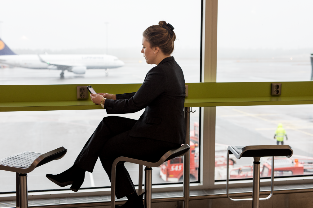 En kvinna sitter vid fönstret i terminalen och tittar på sin telefon