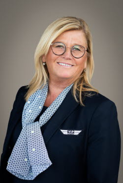 Woman with shoulder length hair and round glasses dressed in suit jacket and scarf smiling at the camera.