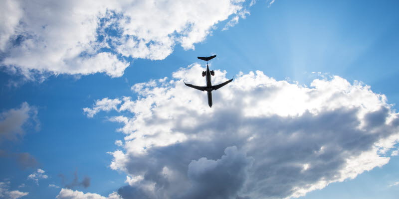 Flygplan i luften mot blå himmel och moln