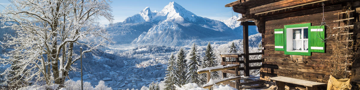 Panoramic view of scenic white winter wonderland mountain scenery in the Alps with traditional old wooden mountain chalets on a beautiful cold sunny day with blue sky and clouds