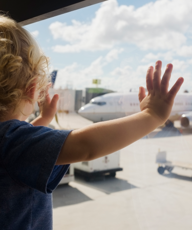 Litet barn står vid ett fönster och tittar på ett flygplan.
