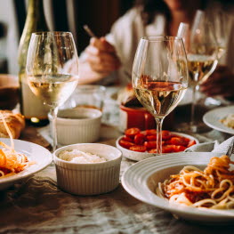 Tallrikar med pastarätter och glas med vitt vin på ett bord.