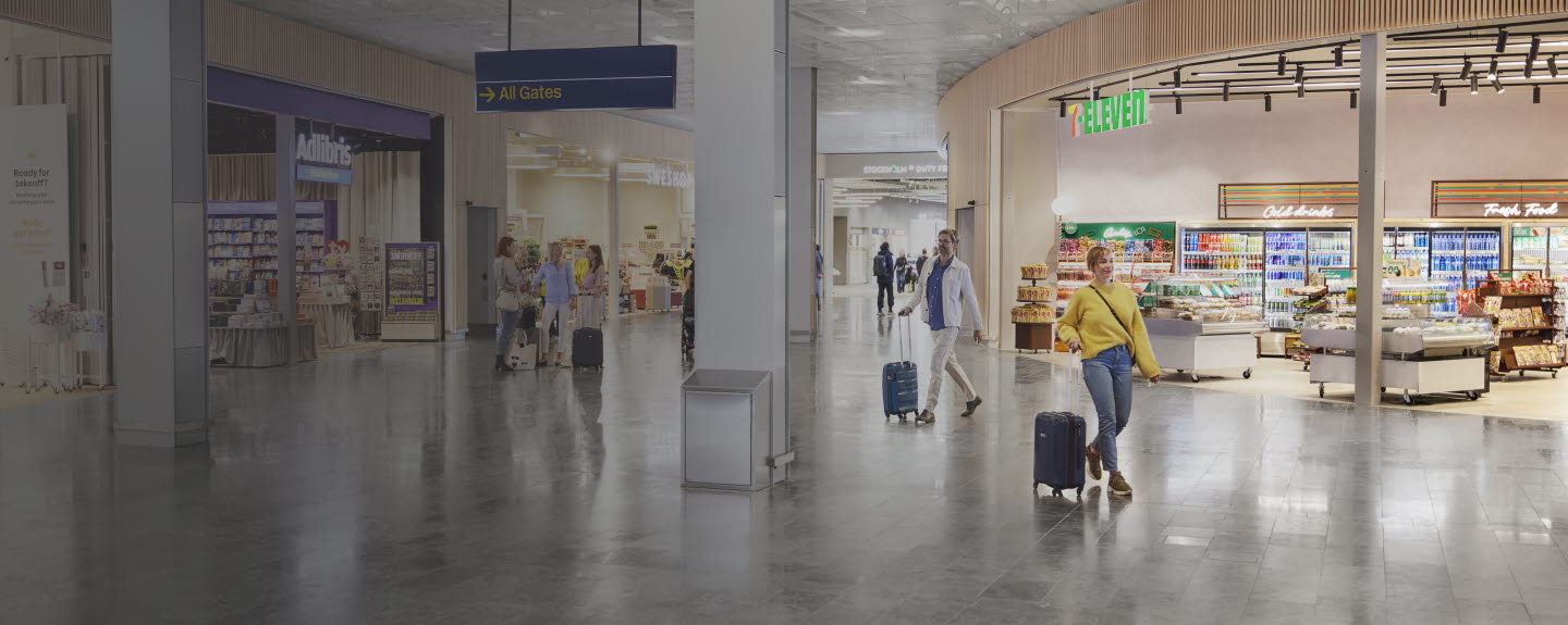 People with suitcases walking and standing in open area between stores.