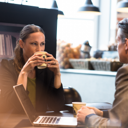 Kvinna och man dricker kaffe med dator på bordet