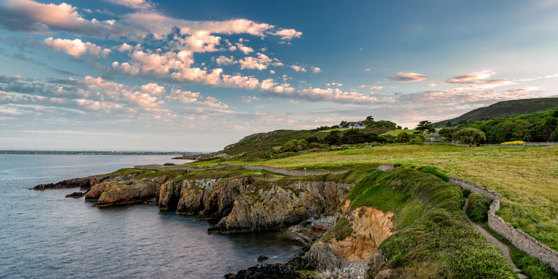 Irländskt landskap med gröna klippor vid vatten och en blå himmel