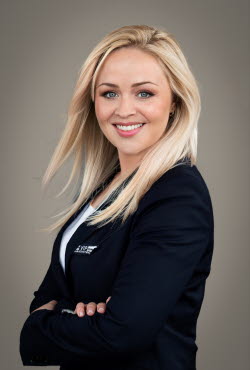 Woman with flowing straight hair dressed in suit jacket has her arms crossed and is smiling at the camera.